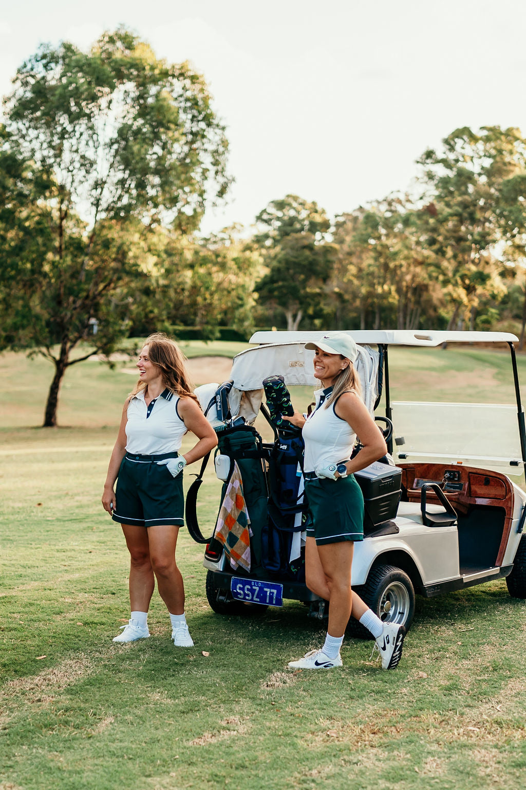two women on course wearing linksy golf next to their golf cart watching a shot