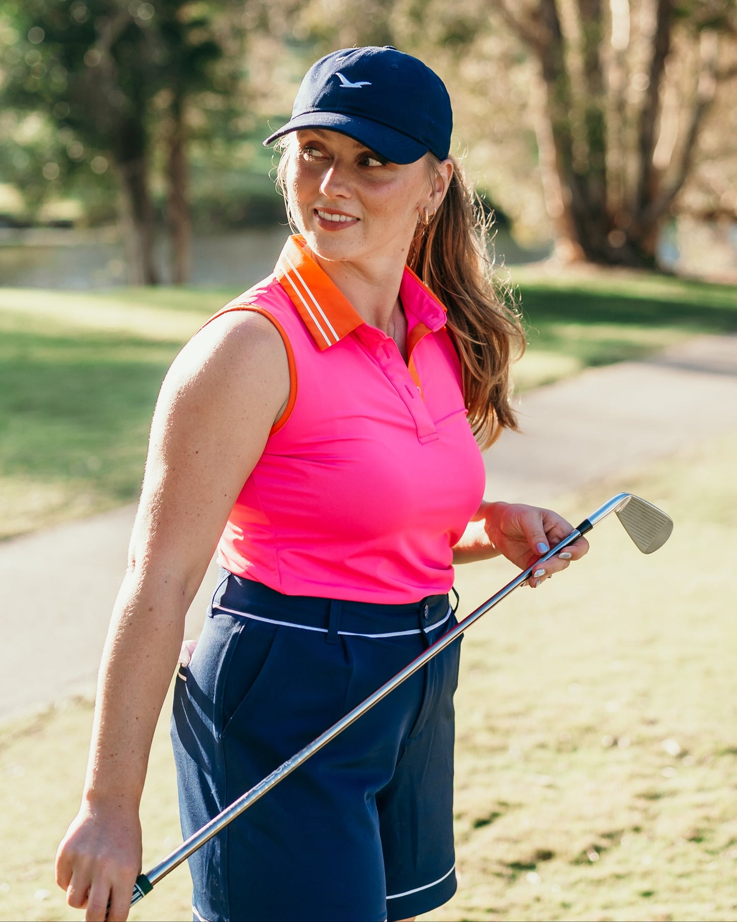 Girl golfer wears linksy gear on courser, stella shorts navy, magrie polo pink and little birdie cap navy