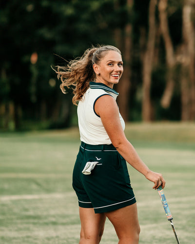 Golfer wearing Margie Polo in white with Evergreen accents and Stella Tailored Golf Shorts, walking the course with confidence and style.