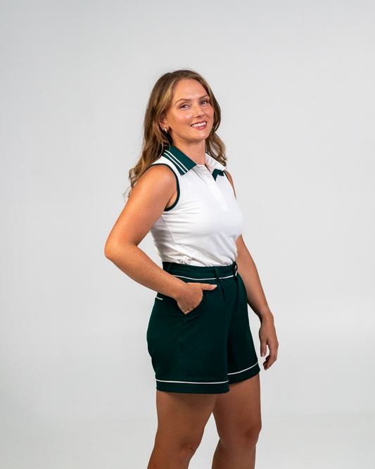 Model wearing Stella Tailored Golf Shorts in Evergreen with Margie Polo (White). High-waisted, fit-and-flare design with contrast piping detail.